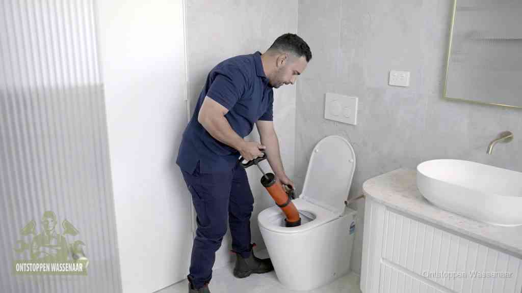 Een monteur buigt over een wandcloset en duwt met de hand een persluchtontstopper in de toiletpot om de verstopping handmatig los te maken in Wassenaar