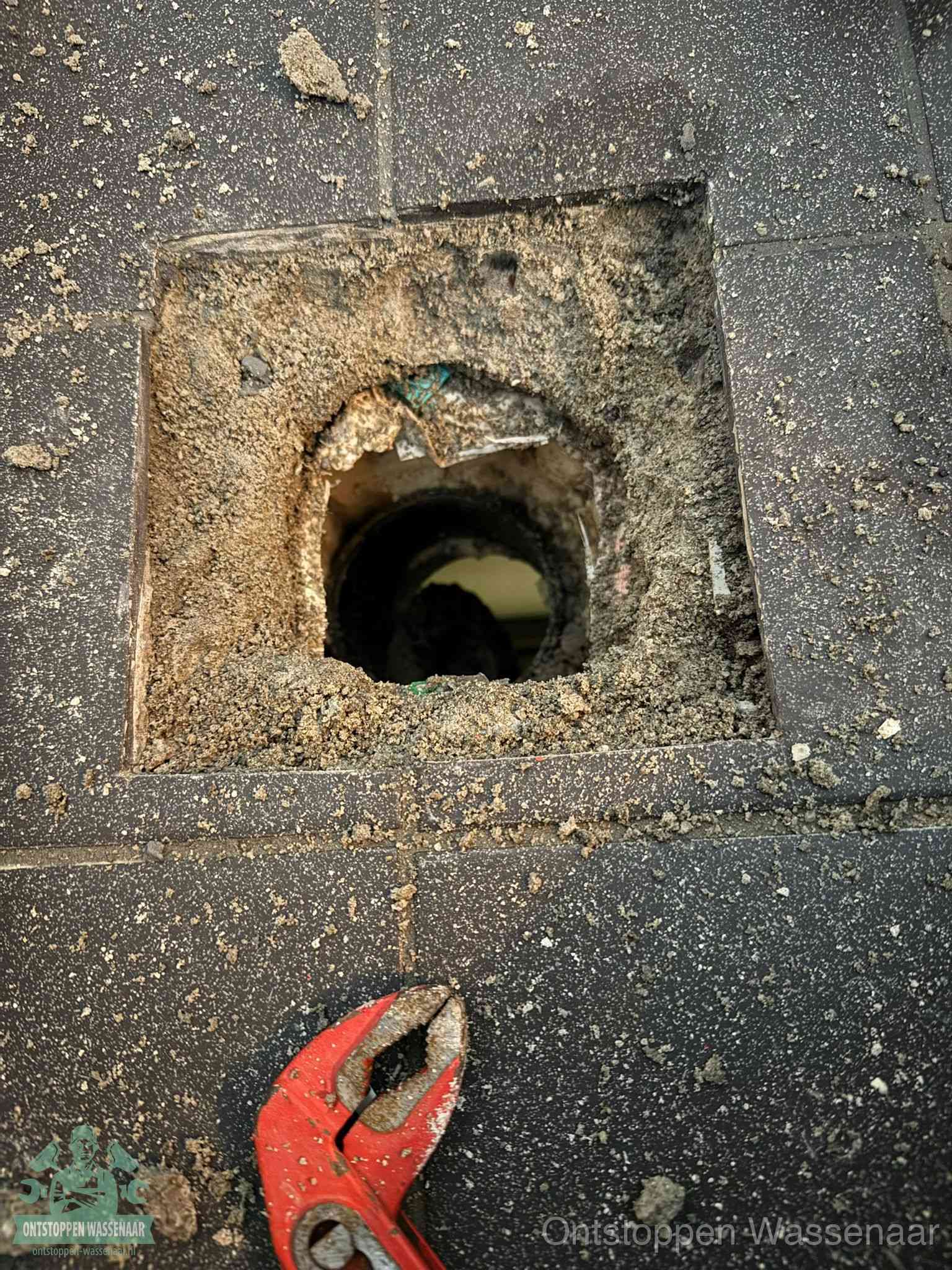 Een geopend rioolputje in een betontegelvloer met losgemaakt rooster en een zichtbare ronde afvoerbuis, het achterhalen waar de afvoerverstopping zit in Wassenaar