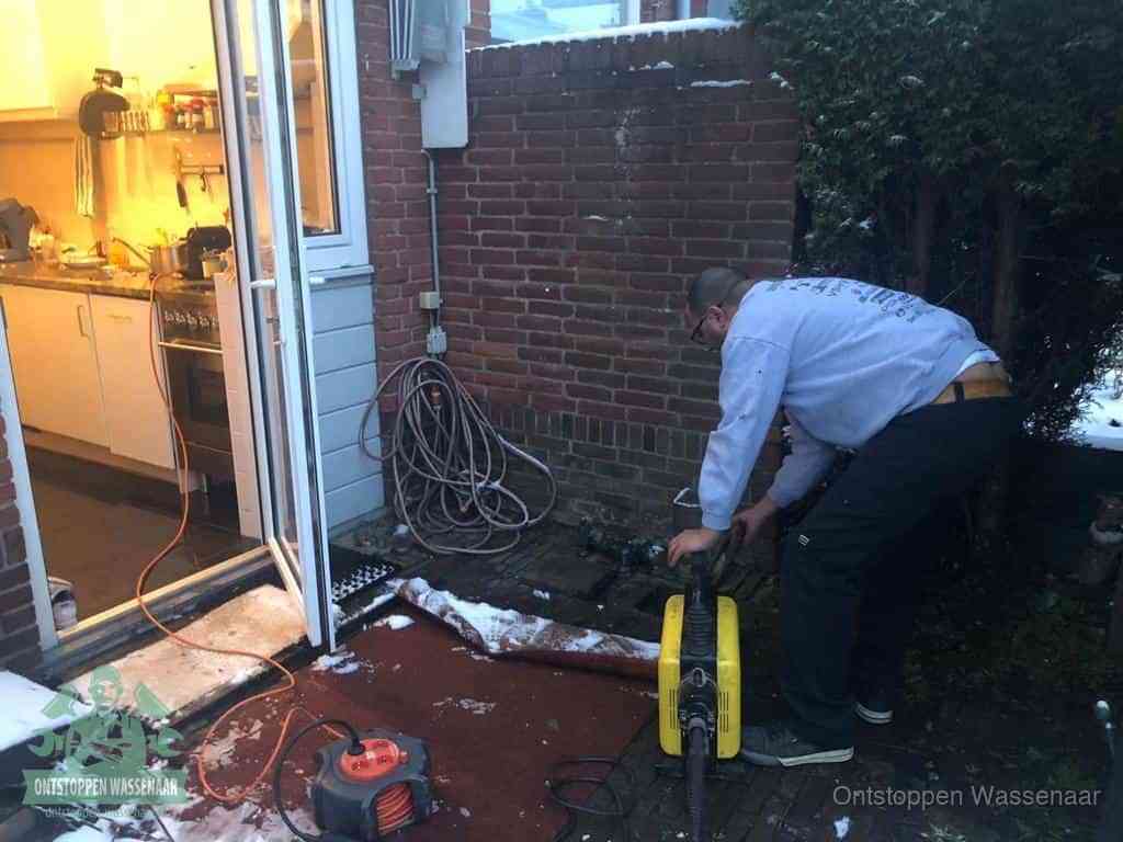 Een monteur werkt buiten bij een open riool-/grondput met een elektrische ontstoppingsmachine om een verborgen afvoerprobleem op te sporen in Wassenaar