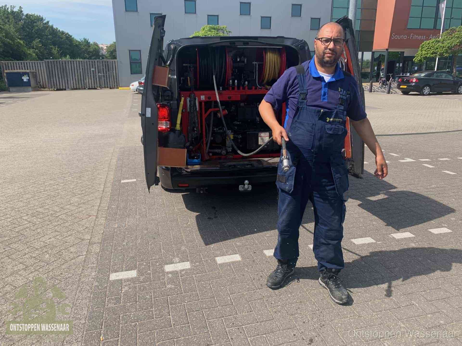 Een monteur bij zijn bestelbus met een hogedruk- en rioolreinigingsunit, klaar om de oorzaak van terugkerende wc-verstoppingen aan te pakken in Wassenaar