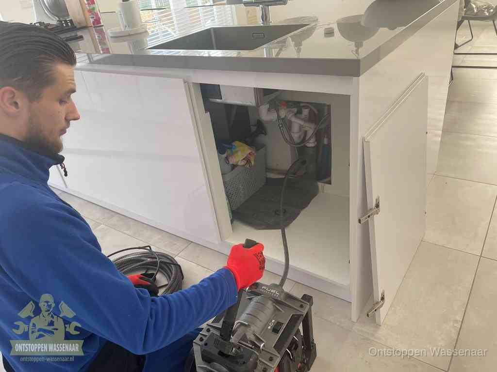 Monteur ontstopt met een veermachine een verstopte afvoer onder de gootsteen in Wassenaar