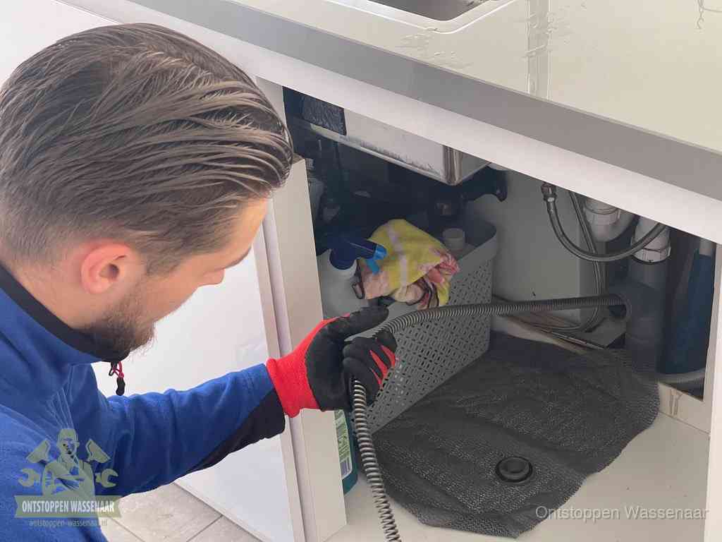 Een monteur voert een flexibele ontstoppingsveer in de afvoer om een verstopping voorbij de bocht van het toilet te bereiken in Wassenaar