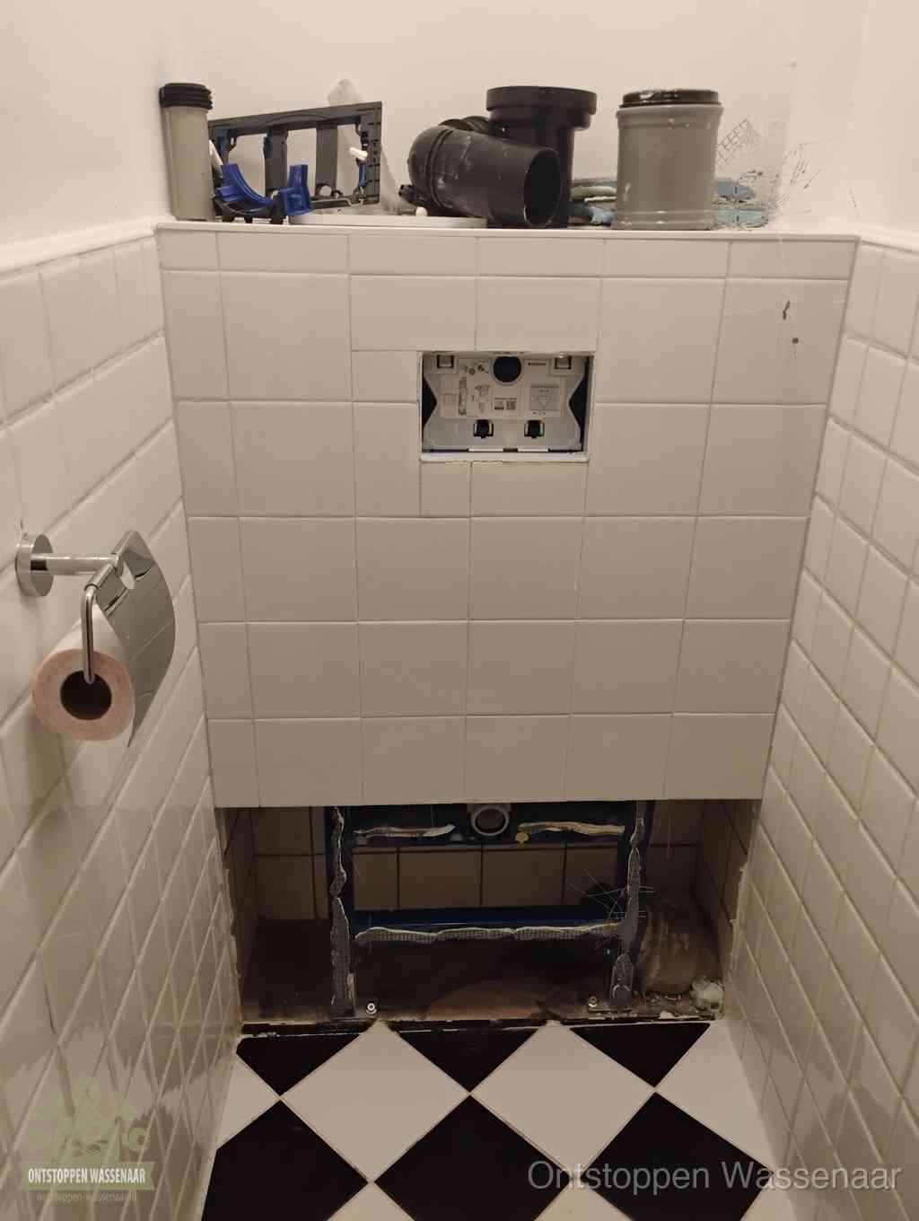 Een toiletruimte waar het hangtoilet en de inbouwreservoir-onderdelen zijn vrijgelegd voor onderhoud, periodiek nazicht voorkomt een wc-verstopping in Wassenaar